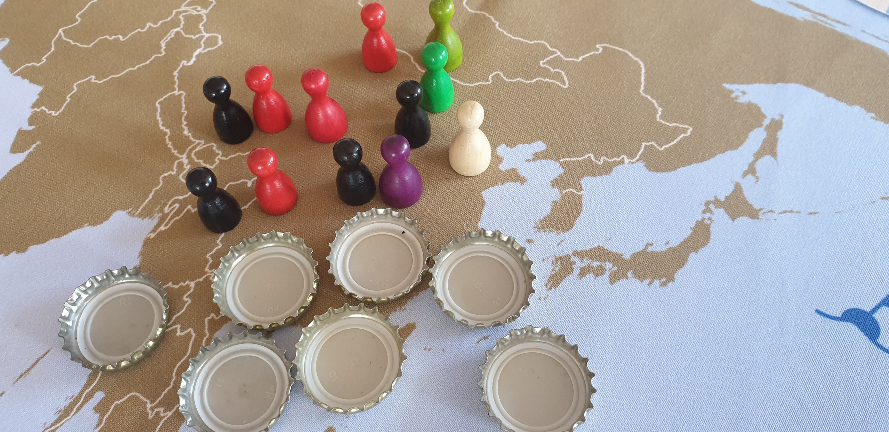 Kronkorken und Spielfiguren auf der Weltspielplane